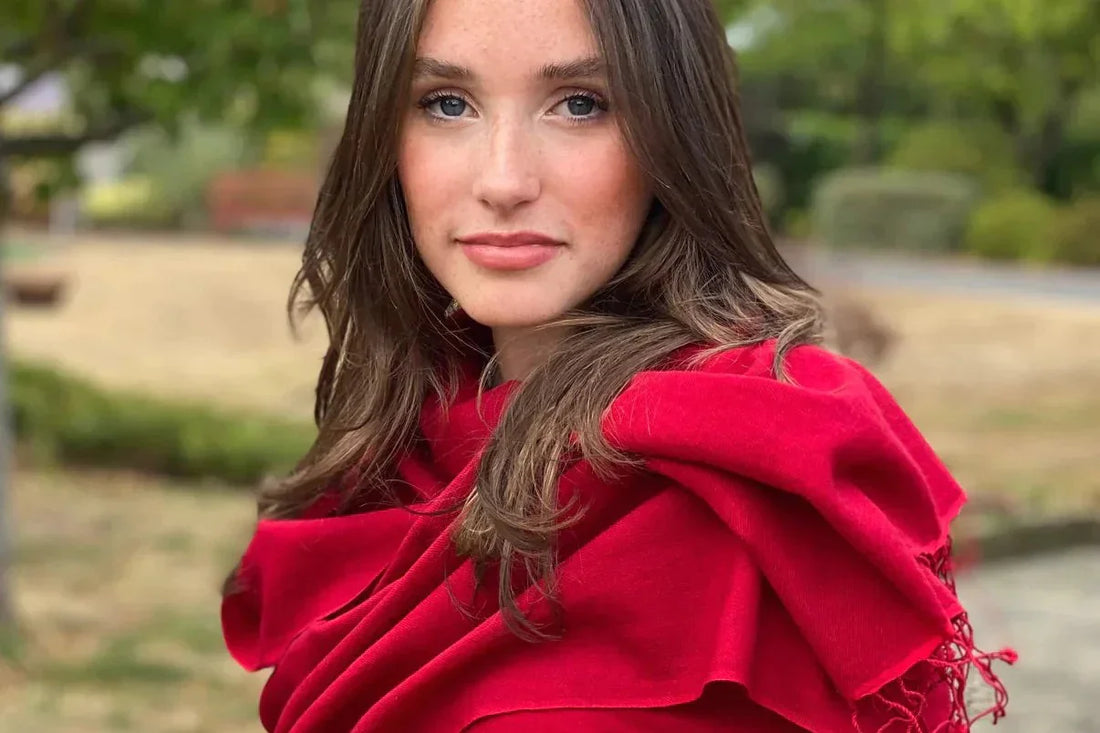  A stylish young lady wearing a red cashmere pashmina, smiling warmly, with a Christmas-decorated fireplace in the background, featuring candles, twinkling lights, and festive decoration