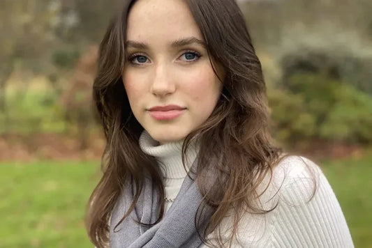 Young woman wrapped in a luxurious grey cashmere scarf around the neck, standing in a vibrant green field
